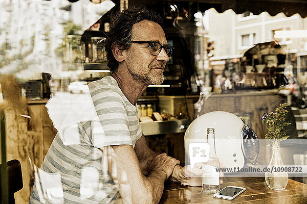 Mann sitzt hinter der Fensterscheibe eines Cafés