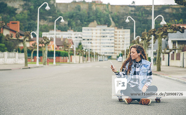 Young woman listening to music sitting on skateboard