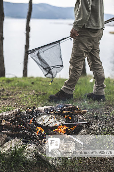 Bulgaria  man frying rudd at camp fire at shore of Dospat Reservoir