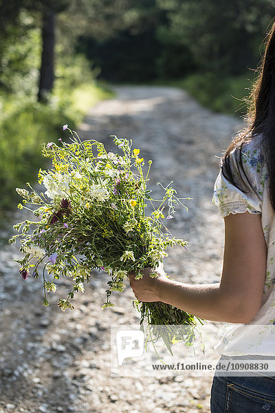 Back view of woman holding bunch of wildflowers