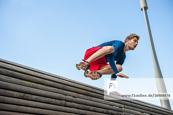 Junger sportlicher Mann beim Springen über eine Bank