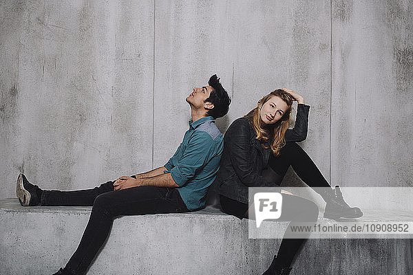 Young couple sitting in front of concrete wall
