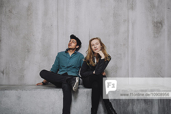 Young couple sitting in front of concrete wall