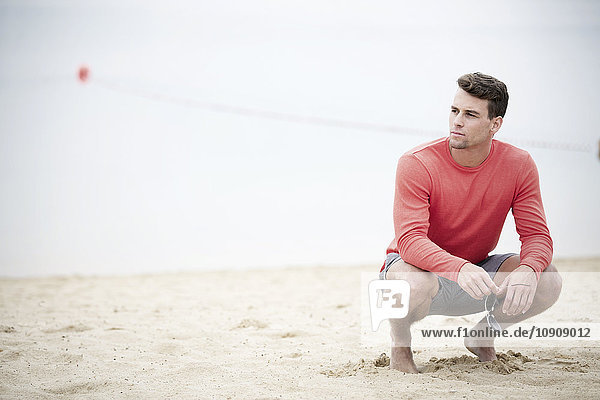 Mann kauernd am Sandstrand vor einem See
