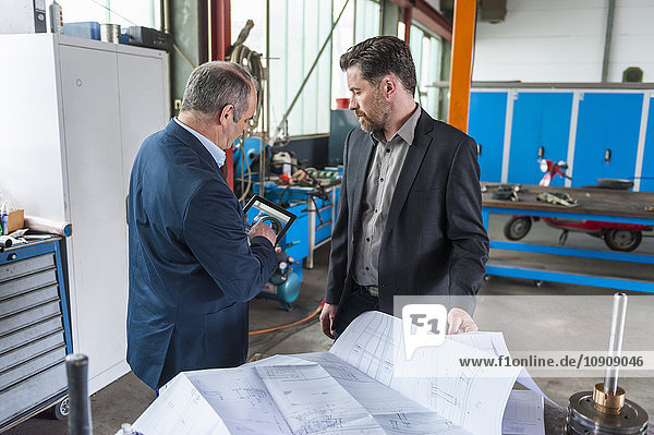 Two engineers with digital tablet  construction plan in front of hydraulic cylinder