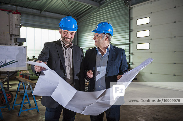 Managers with helmet and construction plan in workshop