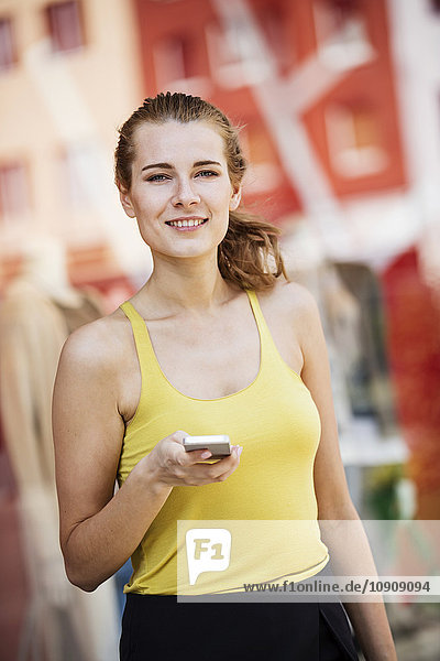 Porträt einer lächelnden jungen Frau mit Handy im Freien