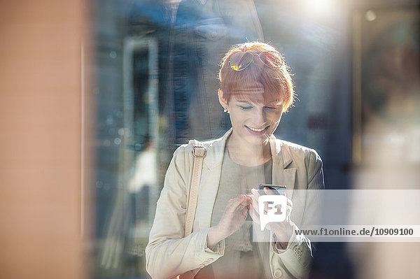 Lächelnde junge Frau mit Handy am Schaufenster