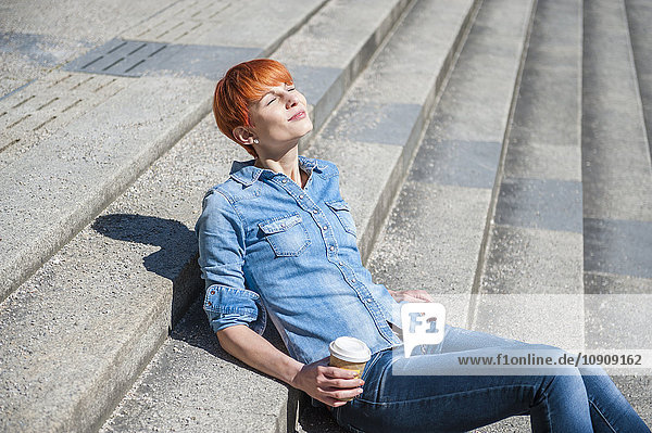 Junge Frau entspannt auf der Treppe mit Kaffee zum Mitnehmen