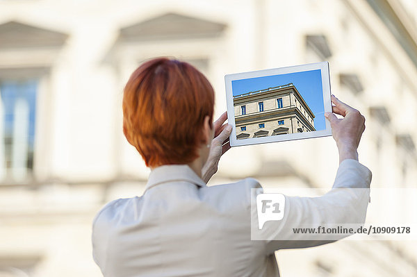 Junge Frau im Freien mit digitalem Tablett beim Fotografieren eines Hauses