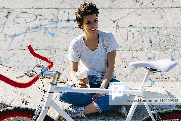 Lächelnde junge Frau mit Fahrrad und Kaffee zum Mitnehmen