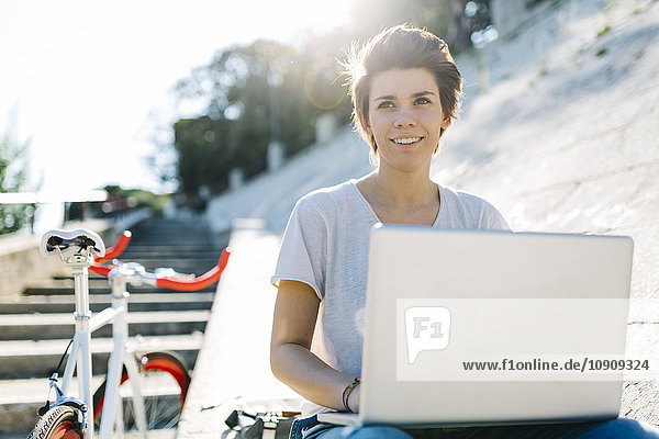 Junge Frau mit Fahrrad im Freien sitzend mit Laptop