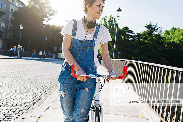 Lächelnde junge Frau schiebt Fahrrad auf Brücke