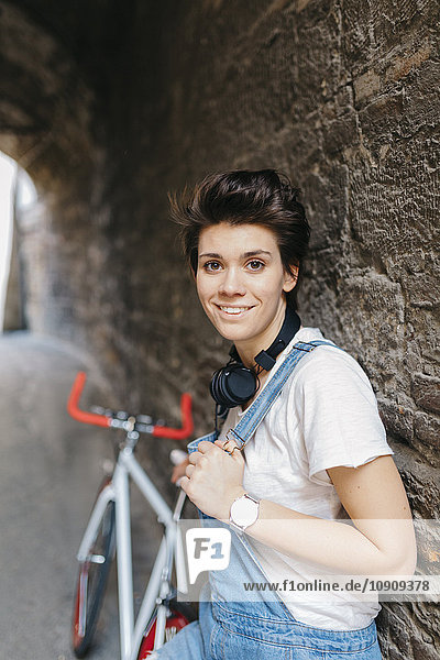 Porträt der lächelnden jungen Frau mit Fahrrad an der Steinmauer