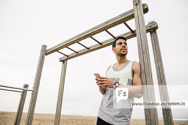 Young man resting at monkey bars on the beach