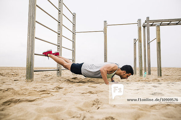 Young man doing push-ups on wall bars on the beach