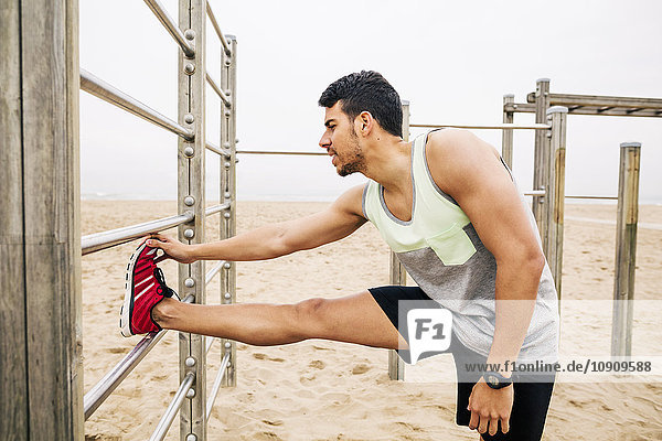 Young man stretching on wall bars on the beach