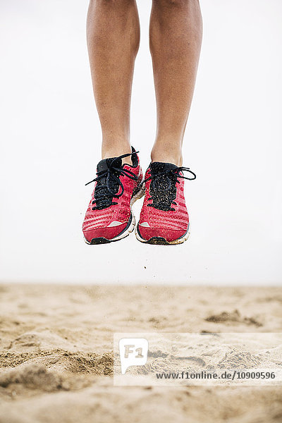 Beine eines Athleten  der mitten in der Luft im Sand springt.