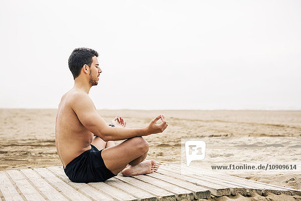 Junger Mann beim Yoga an der Strandpromenade