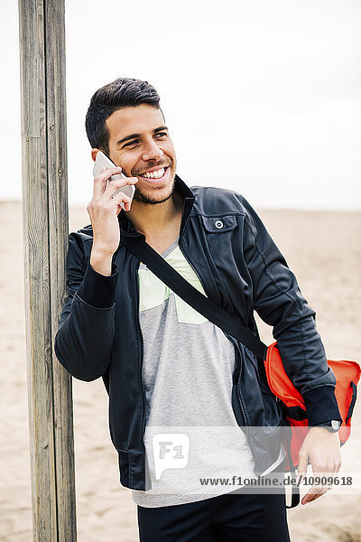Lächelnder junger Mann am Handy am Strand