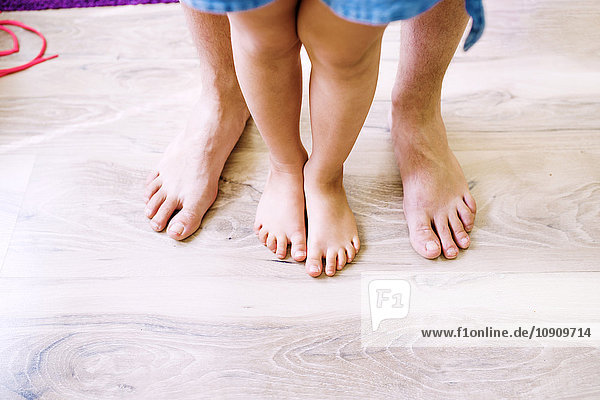 Nackte Beine von Vater und Tochter auf Holzboden stehend