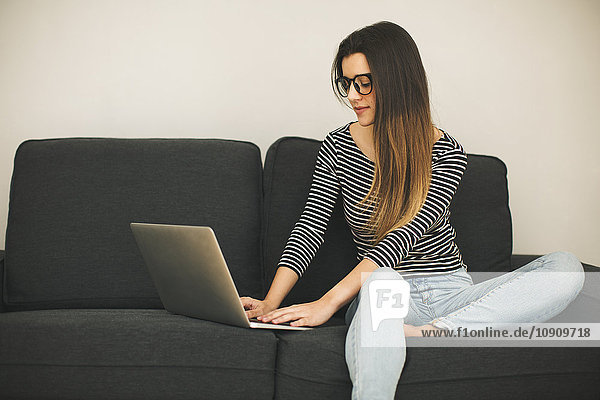 Junge Frau sitzt auf der Couch mit Laptop