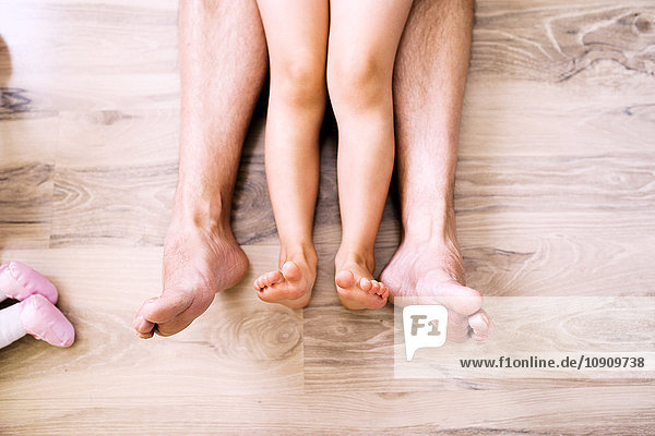 Nackte Beine von Vater und Tochter auf Holzboden sitzend