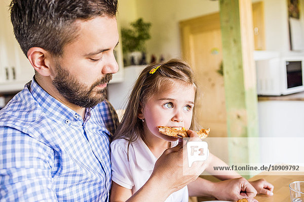 Vater füttert seine kleine Tochter mit Pizza.