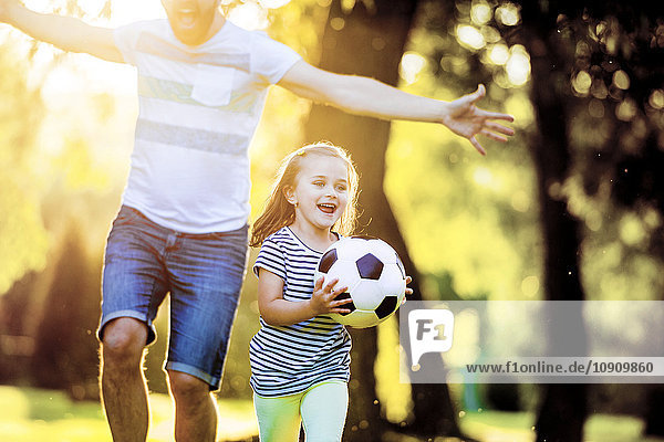 Glückliches kleines Mädchen mit Fußball  das mit seinem Vater im Park spielt.