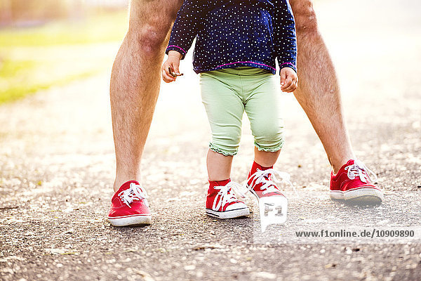 Die Beine des kleinen Mädchens und ihres Vaters tragen beide rote Turnschuhe.