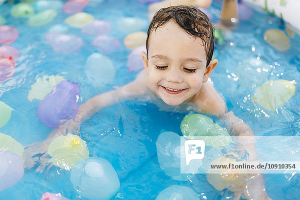 Lächelnder kleiner Junge spielt mit Wasserballons im Pool