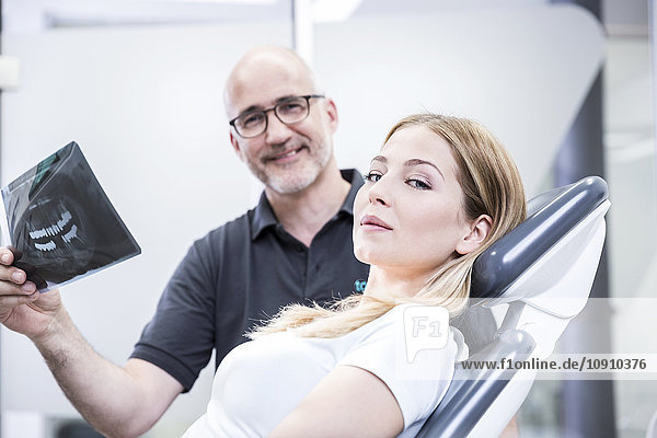 Zahnarzt  der dem Patienten ein Röntgenbild zeigt  auf dem Zahnarztstuhl sitzend
