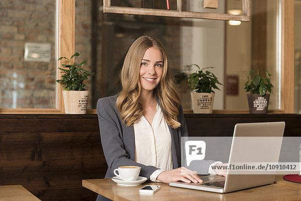Porträt einer lächelnden jungen Frau mit Laptop im Coffee-Shop