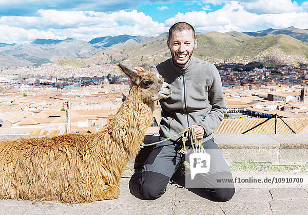 Peru  Cusco  Porträt eines fröhlichen Touristen  der neben Lama kniet