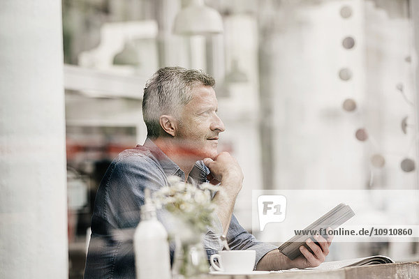Erwachsener Mann sitzt im Café und liest E-Book