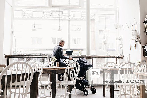 Geschäftsmann sitzend im Café mit Kinderwagen