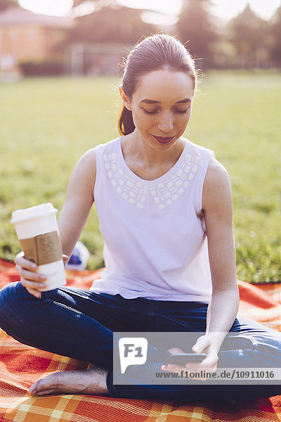 Student im Park bei einem Kaffee zum Mitnehmen  Blick auf das Smartphone