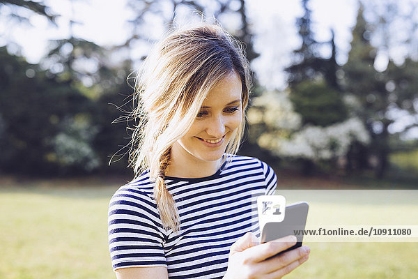 Porträt einer lächelnden  blonden Frau  die ihr Smartphone ansieht.