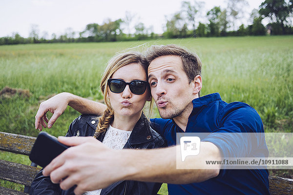 Porträt eines Paares mit schmollenden Mündern  das sich mit dem Smartphone selbst verschlingt.