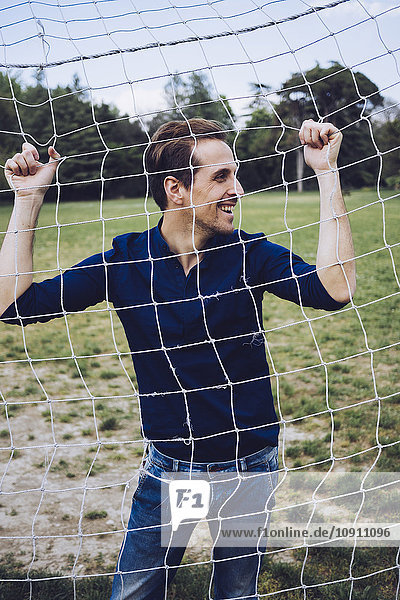 Lachender Mann steht hinter dem Fußballnetz