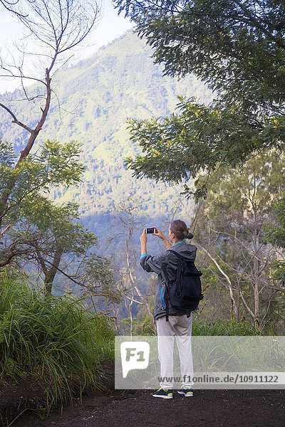 Indonesia  Java  Woman hiking in mountains and taking pictures with smart phone
