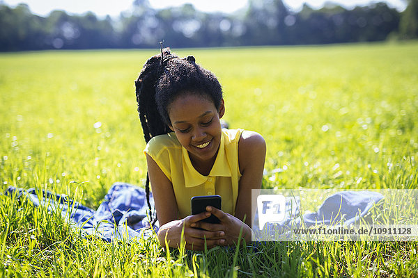 Porträt einer jungen Frau mit Smartphone  die sich auf einer Wiese ausruht