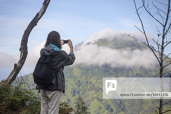 Indonesien  Java  Frau beim Bergwandern und Fotografieren mit dem Smartphone