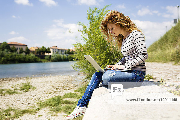Frau mit Laptop am Flussufer