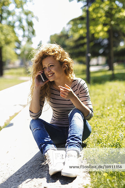 Porträt einer glücklichen Frau beim Telefonieren mit dem Smartphone im Park
