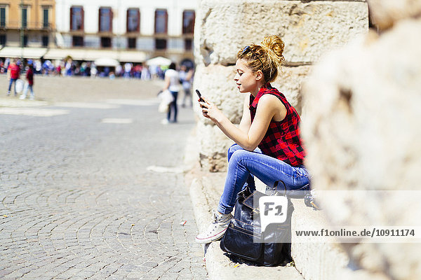 Italien  Verona  Frau sitzt auf der Treppe und schaut auf das Handy.