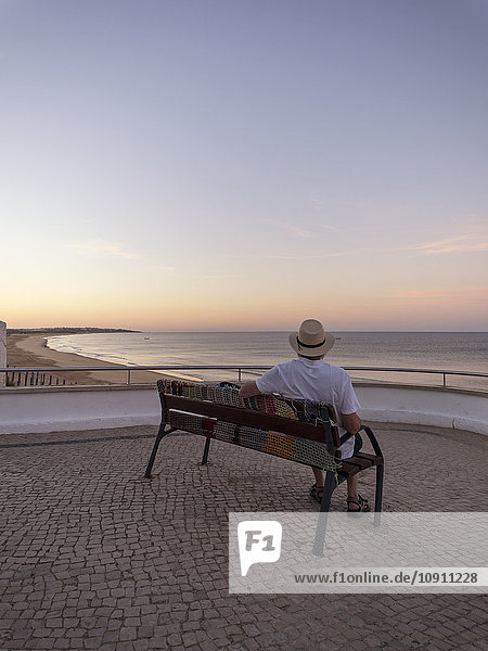 Portugal  Senior sitzt auf der Bank und beobachtet den Sonnenaufgang.