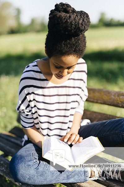 Junge Frau sitzt auf einer Parkbank und liest ein Buch.