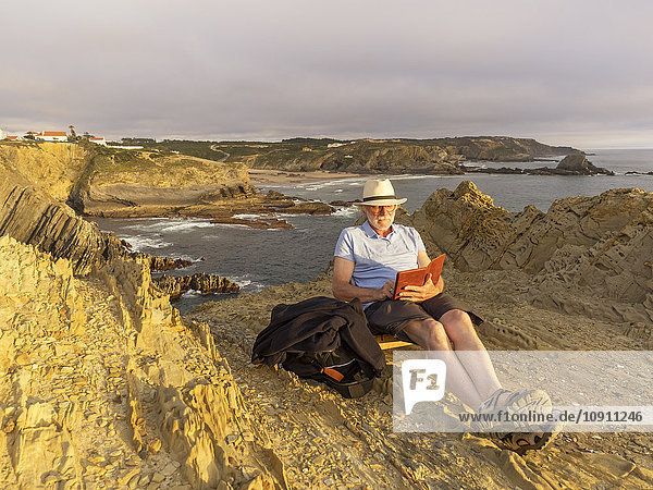 Portugal  Senior man sitting at beach  reading book
