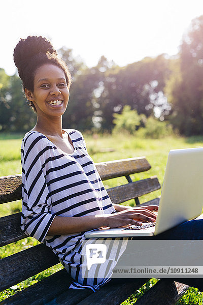 Porträt einer jungen Frau auf einer Parkbank mit Laptop
